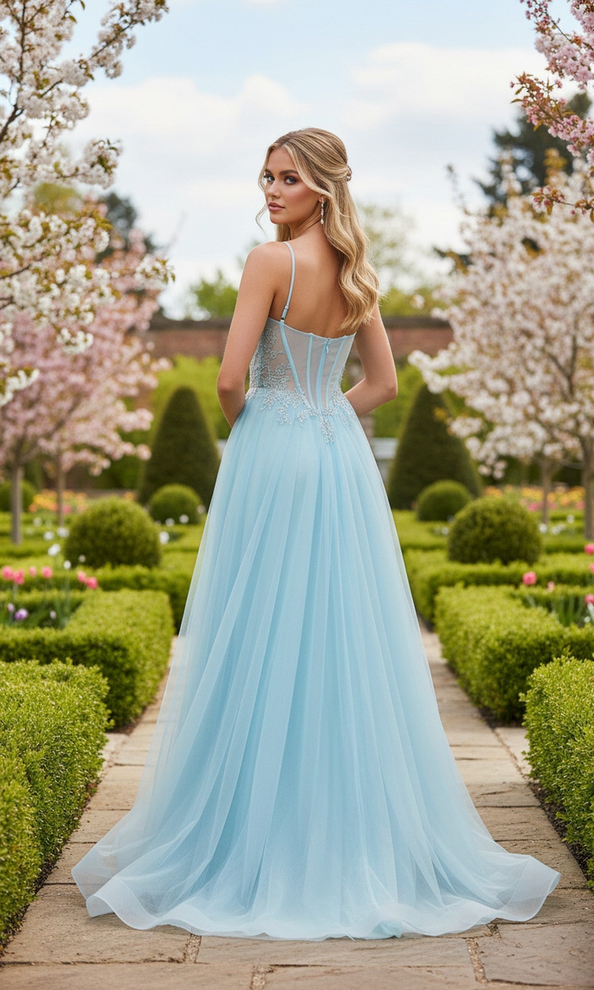 Wearing the La Femme 33436 long prom dress, a woman in a light blue, floor-length sleeveless gown with an embellished corset bodice stands on a stone path in a formal garden with blooming trees and trimmed hedges.